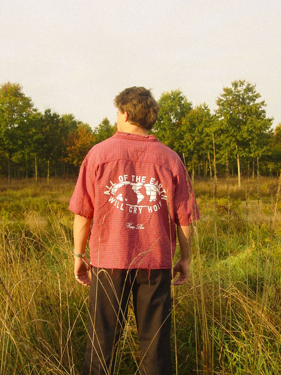 Jaxon in a red flannel, back print: All of the Earth Will Cry Holy